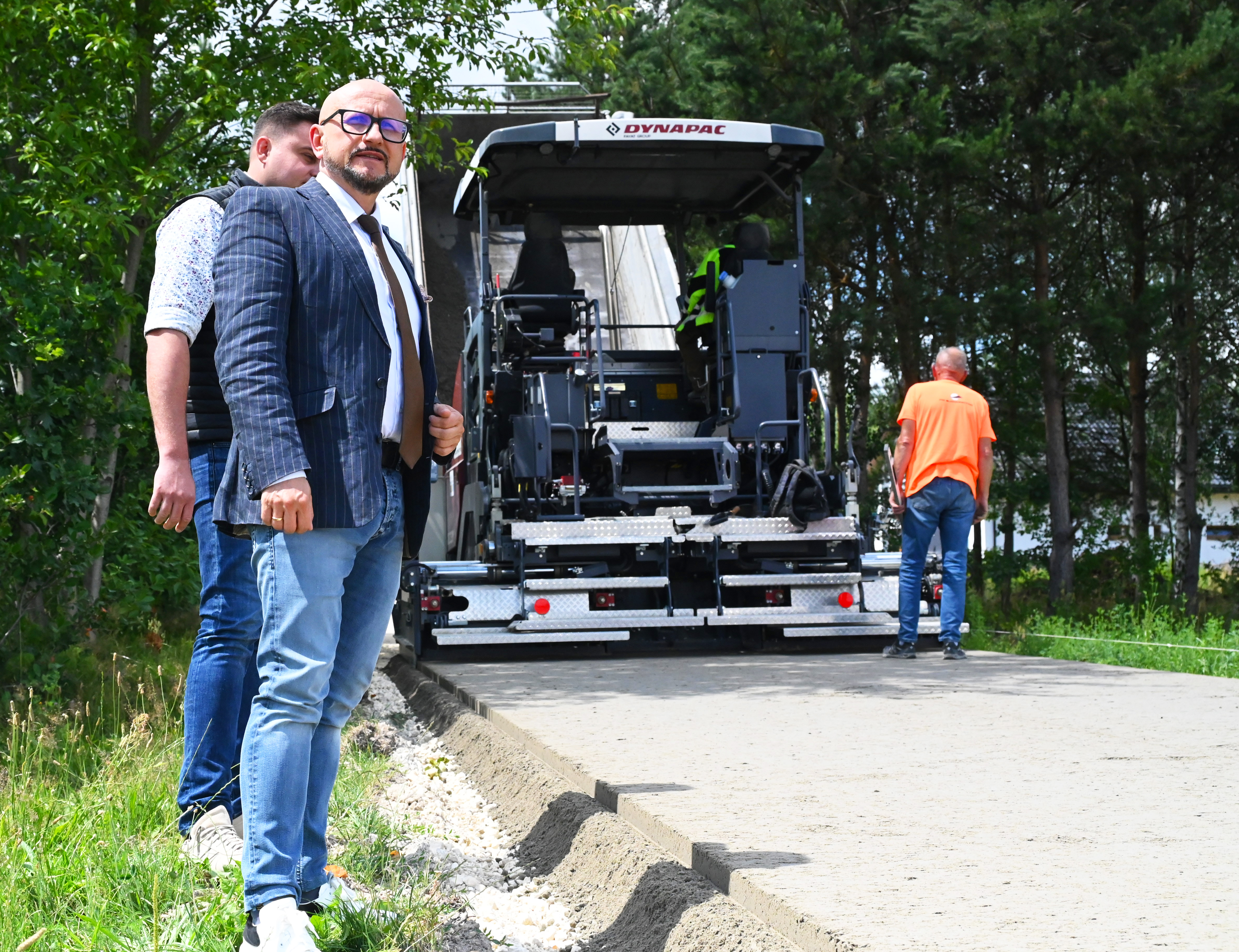 maszyna rozkłada beton na&nbsp;drodze, na&nbsp;pierwszym planie w&oacute;jt konrad koc, za nim mateusz rogut prezes gminnej sp&oacute;łki
