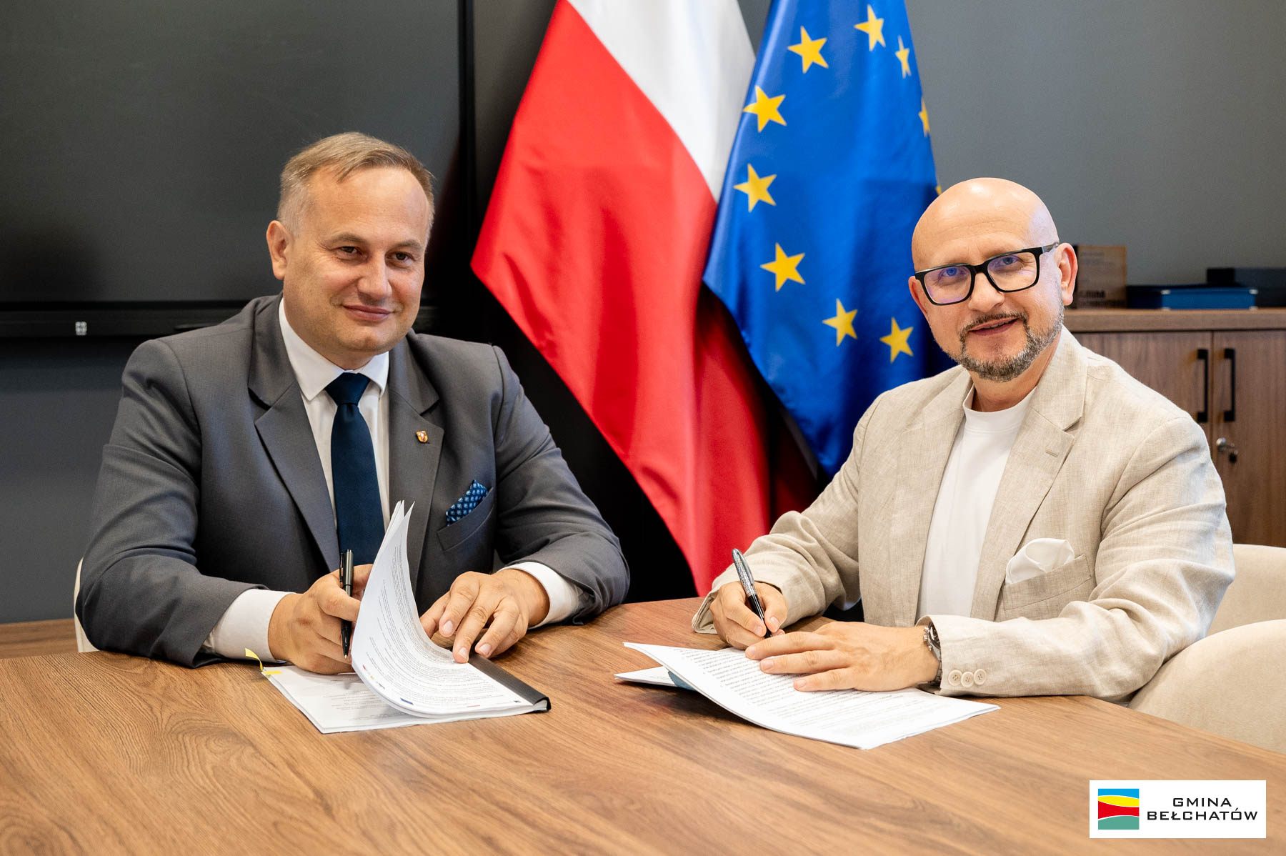 wicemarszałek piotr wojtysiak i&nbsp;w&oacute;jt konrad koc siedzą przy stole i&nbsp;podpisują dokumenty. W tle flaga polska i&nbsp;flaga unijna