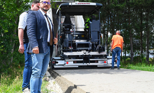 maszyna rozkłada betonową nawierzchnię na gminnej drodze, na pierwszym planie mężczyzna wójt konrad koc, za nim prezes gminnej spółki komunalnej mateusz rogut
