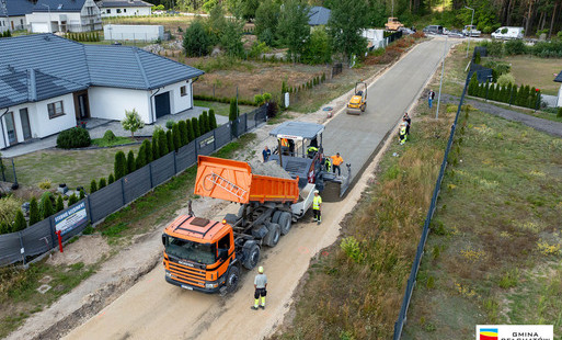 widok z lotu ptaka na osiedlową uliczkę, maszyny budowlane rozkładają betonową nawierzchnię