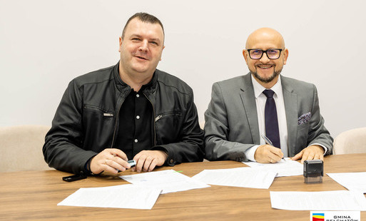 dwaj panowie siedzą przy stole i podpisują umowę, na zdjęciu wójt konrad koc i daniel wrzochol