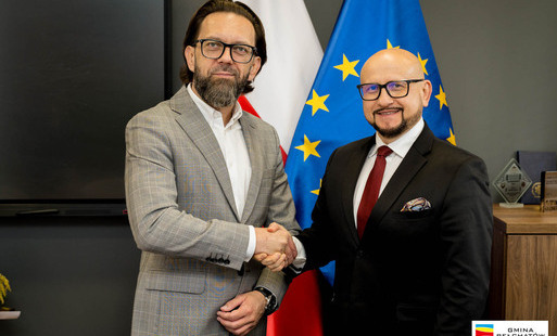 dariusz stępczyński i konrad koc ściskają sobie dłonie. w tle flaga unijna i flaga polska