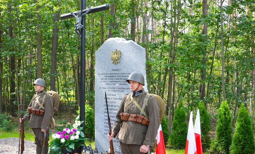 mężczyźni w mundurach wojskowych stoją przy pomniku w kalisku, w tle las